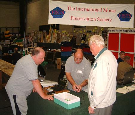 Photograph of Leicester 2009 FISTS stand showing Paul M0BMN, John M0CDL and Keith G3KYF discussing a tiny Australian straight key